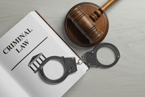 Handcuffs, gavel, and criminal law book symbolizing the work of a criminal defense lawyer.