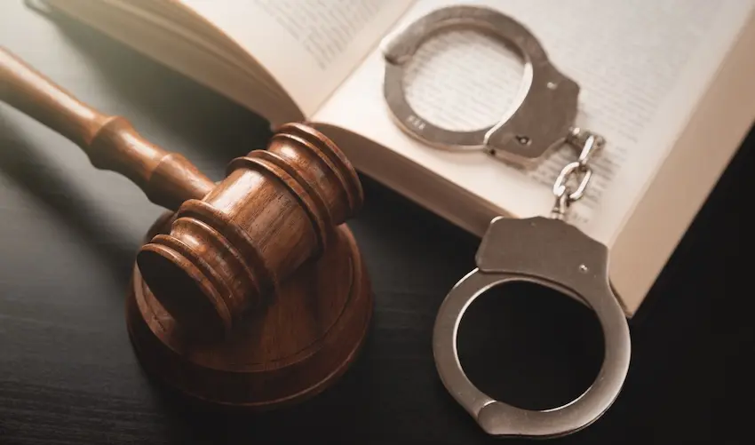 A wooden judge's gavel beside metal handcuffs on an open law book representing criminal defense strategies and legal representation at Byron Pugh Legal.