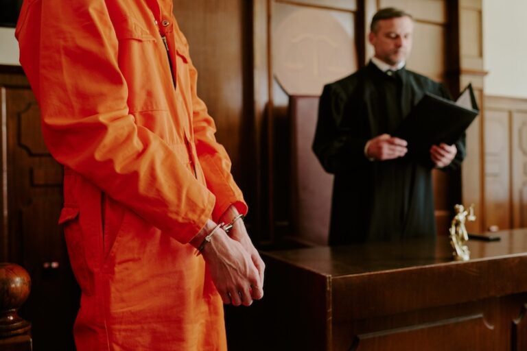 A handcuffed defendant in an orange jumpsuit stands before a judge in black robes reading from a folder in a wood-paneled courtroom representing the high-stakes sentencing phase where criminal defense outcomes can significantly impact a defendant's future in Tennessee.