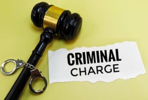 A black judge's gavel and a pair of handcuffs rest on a yellow surface beside a torn piece of paper printed with the words "Criminal Charge" directly illustrating the serious legal consequences that accompany criminal charges in a court of law in Tennessee.