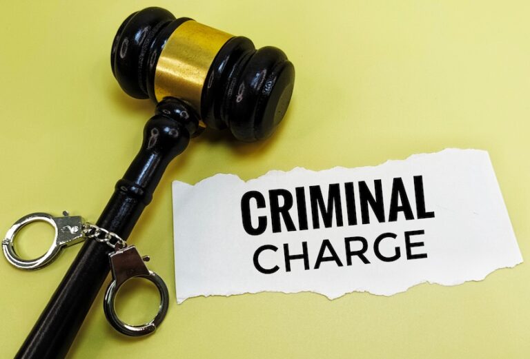 A black judge's gavel and a pair of handcuffs rest on a yellow surface beside a torn piece of paper printed with the words "Criminal Charge" directly illustrating the serious legal consequences that accompany criminal charges in a court of law in Tennessee.
